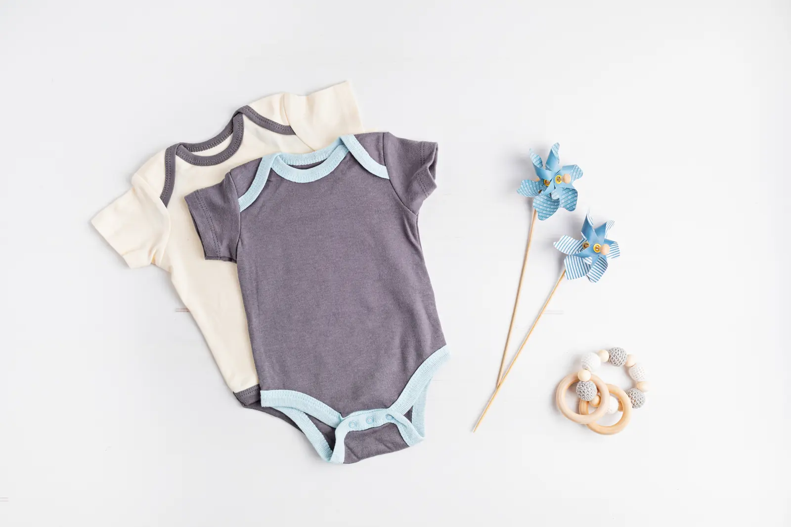 Dois bodies de manga curta lado a lado, um cinza com debrum azul-claro e um creme, com cata-ventos azuis