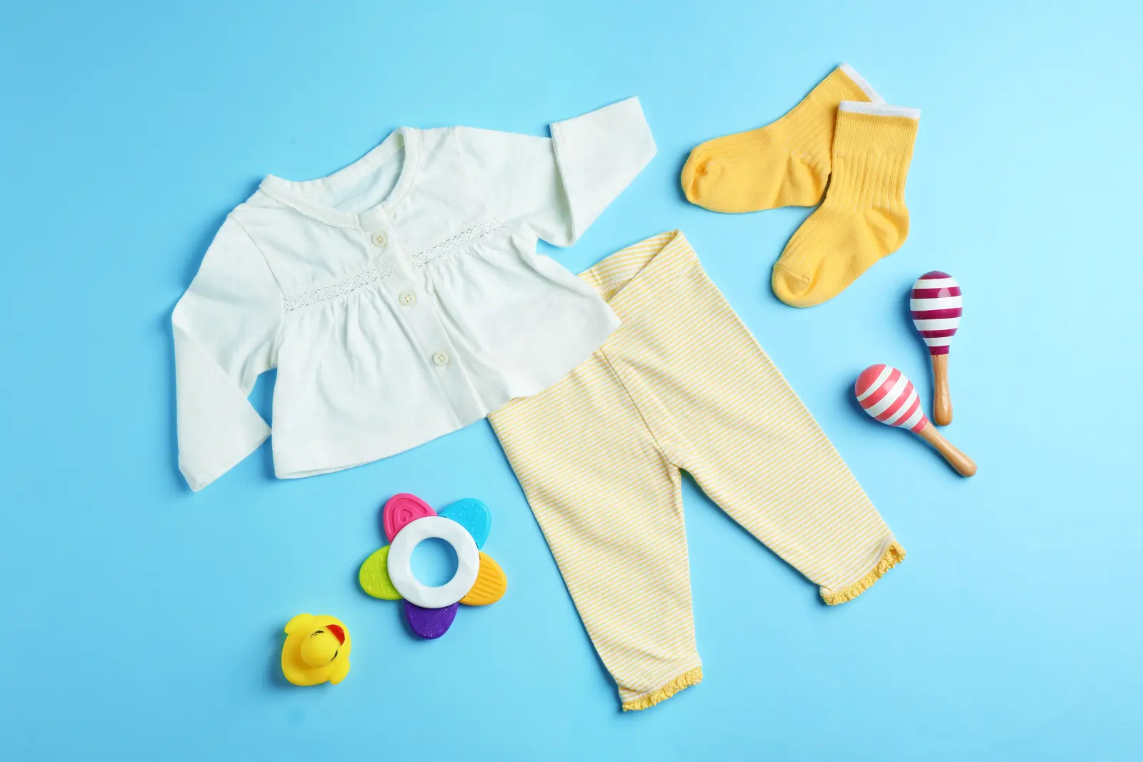 Bata branca de manga longa com botões, legging listrada amarela, meias amarelas e chocalhos coloridos sobre fundo azul